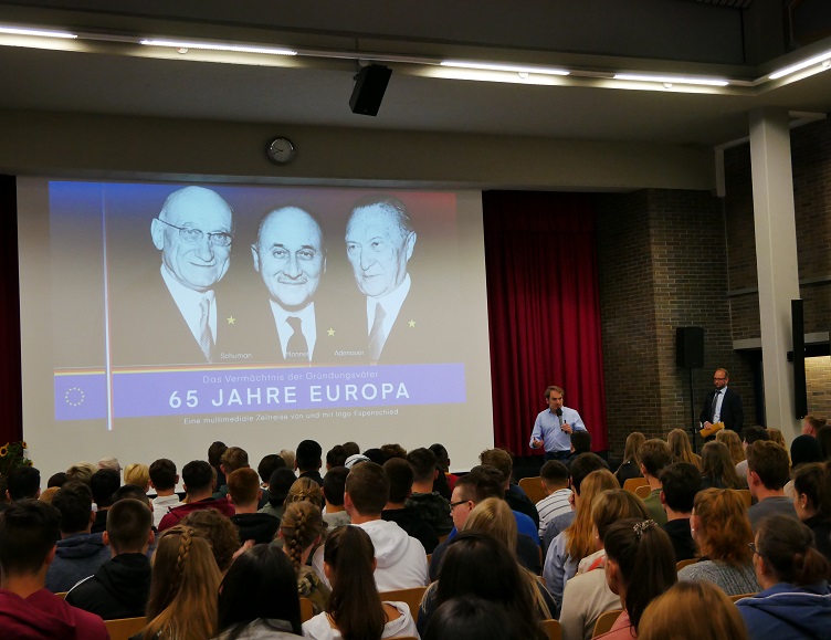 Veranstaltung zur Europaschule/Europa: Aula mit Publikum, vorn Vortragende; auf der Leinwand „65 Jahre Europa“.