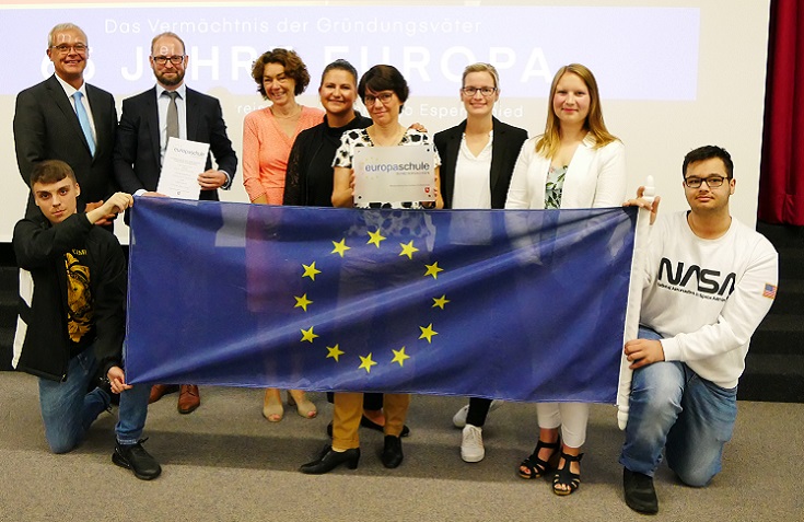 Erwachsene und Jugendliche halten eine Europaflagge sowie ein Schild mit dem Schriftzug "Europaschule" hoch. 