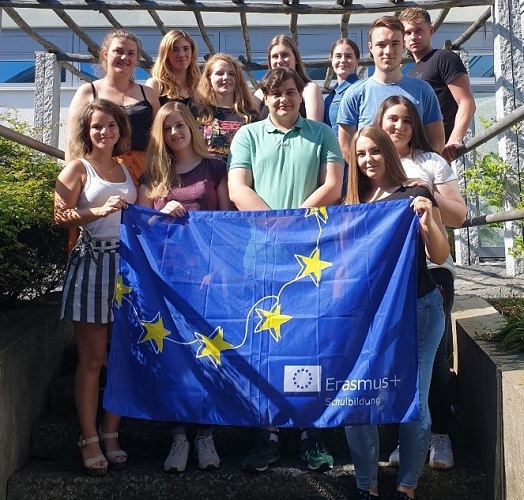 Gruppenfoto jugendlicher mit einer Erasmus+ Flagge in einem sonnigen Innenhof. 