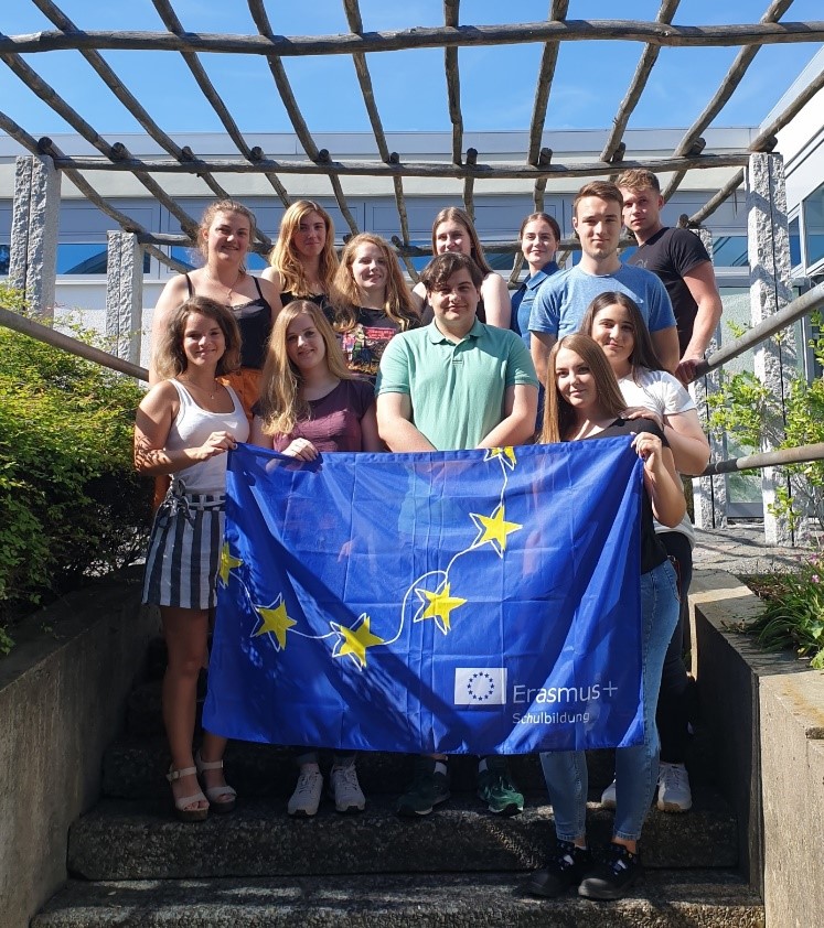Gruppenfoto jugendlicher mit einer Erasmus+ Flagge in einem sonnigen Innenhof. 