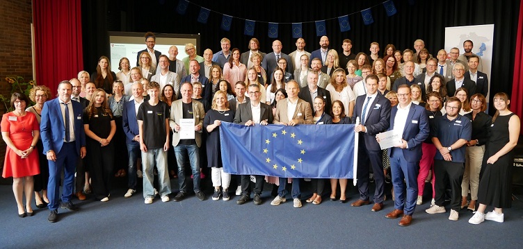 Gruppenbild von schick angezogenen Erwachsenenen und Jugendlichen, die europ&auml;ische Flagge haltend. 