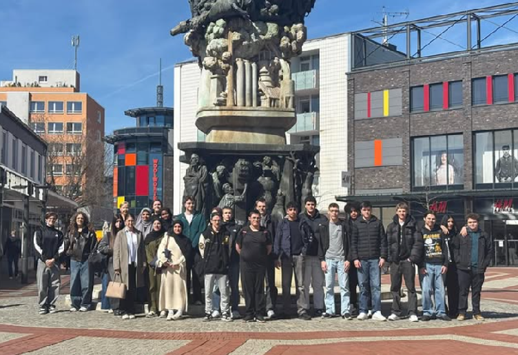 Gruppenbild: Jugendliche vor einer Statue, auf einem sonnigen Platz in der Stadt. 