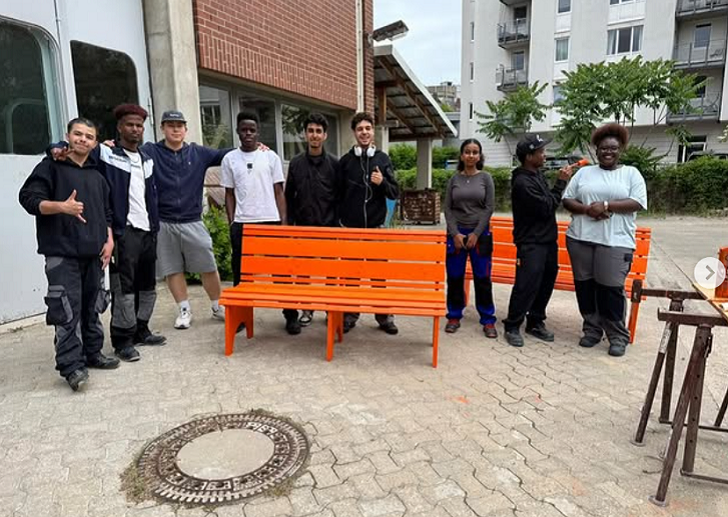 Eine Gruppe Schüler posiert um eine orangene Holzbank herum. 