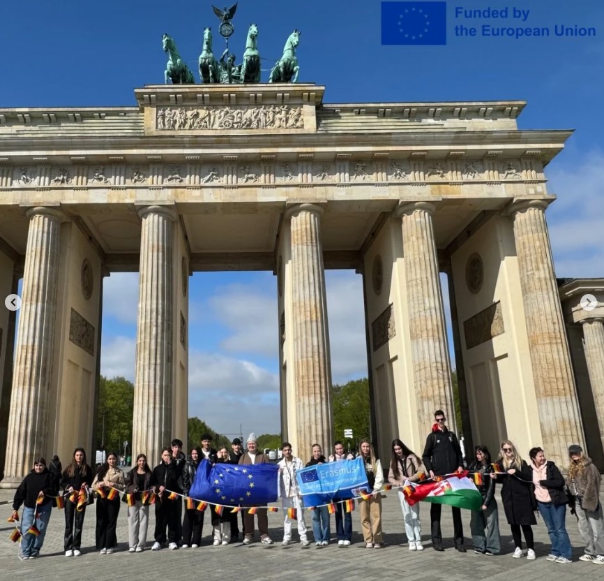 Schülergruppe vor dem Brandenburger Tor. Oben rechts steht: ‘Funded by the European Union’ mit EU-Flagge.