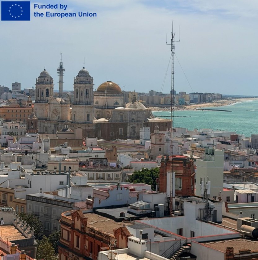 Panoramablick über eine Küstenstadt mit großer Kathedrale; im Hintergrund Strand und Meer. Oben links steht: ‘Funded by the European Union’ mit EU-Flagge.