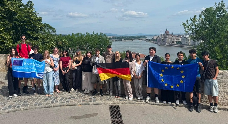 Ein sonniges Gruppenbild des Schüleraustauschs nach Ungarn. Die Schüler halten eine Erasmus-, eine Deutschland-, und eine Europa-Flagge hoch. 