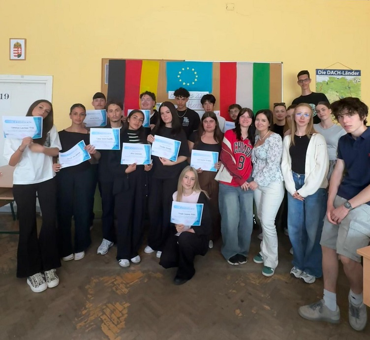 Ein Gruppenbild des Schüleraustauschs nach Ungarn. Die Schüler halten Papierzettel hoch, stehen in einem Schulgebäude.