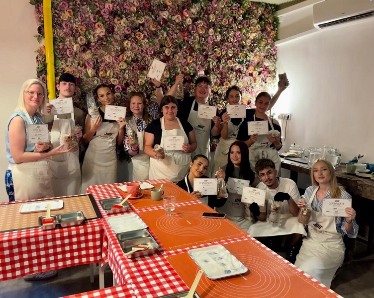 Ein Gruppenbild des Schüleraustauschs nach Ungarn. Die Schüler halten Zertifikate in einem Restaurant hoch. Sie haben alle Schürzen um.  