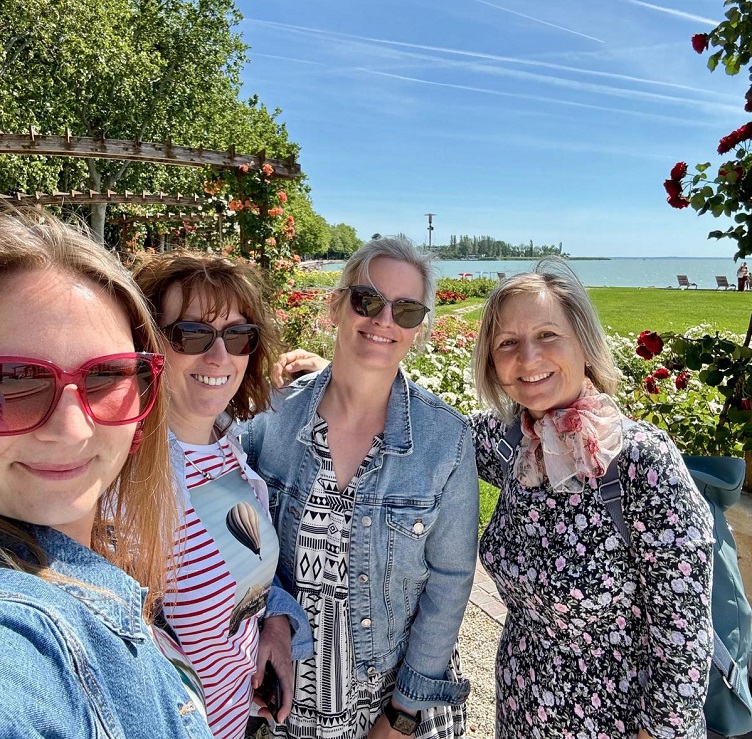 Selfie von drei lachenden Frauen und einem Mädchen vor einem See. Alle haben Sonnenbrillen auf, die Sonne scheint. 