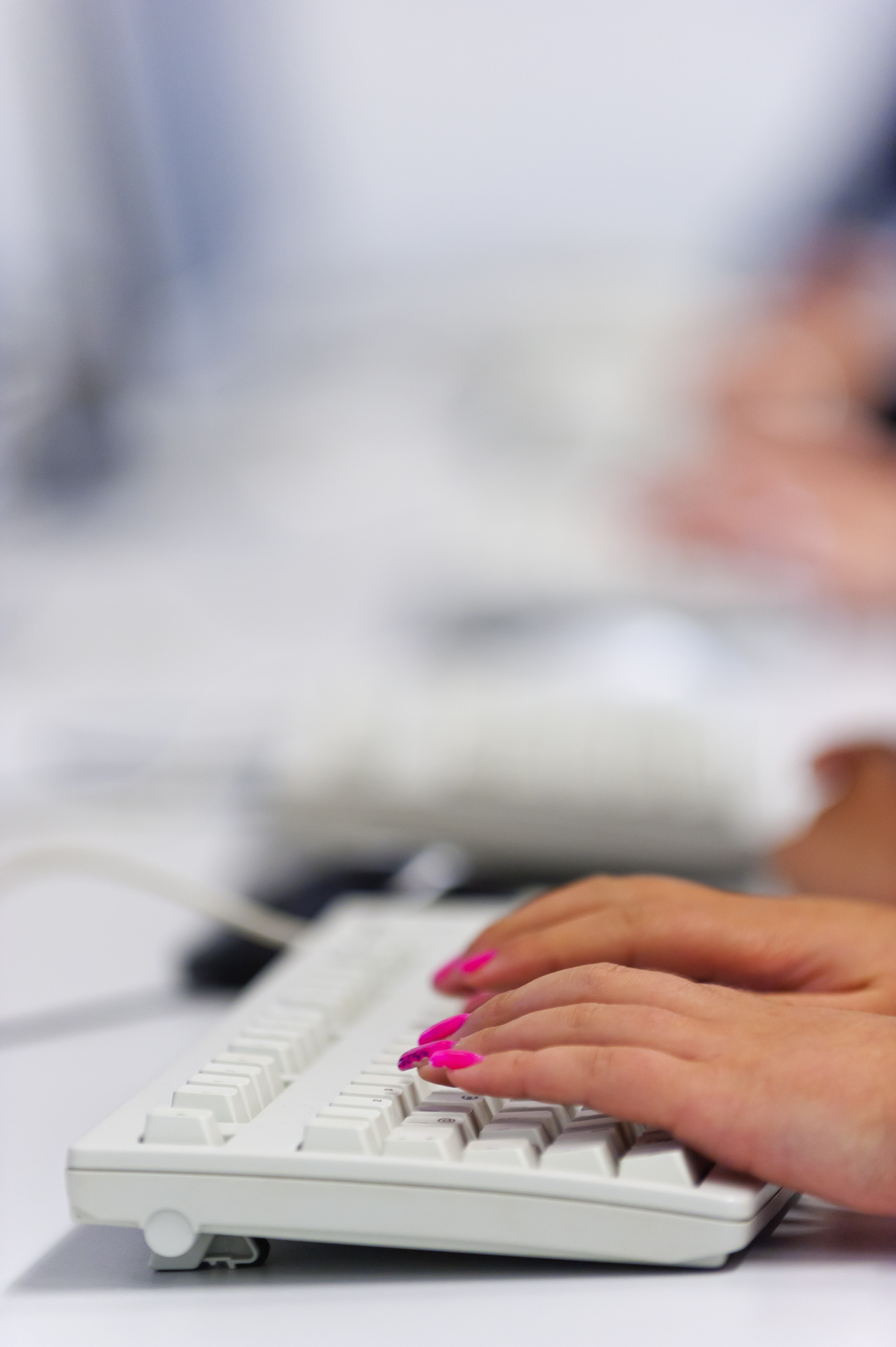 Gepflegte Hände mit langen rosa Fingernägeln tippen auf einer Computertastatur. 