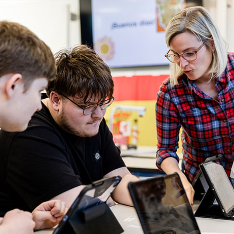Eine Lehrerin erkl&auml;rt zwei Sch&uuml;lern mit iPads etwas. 