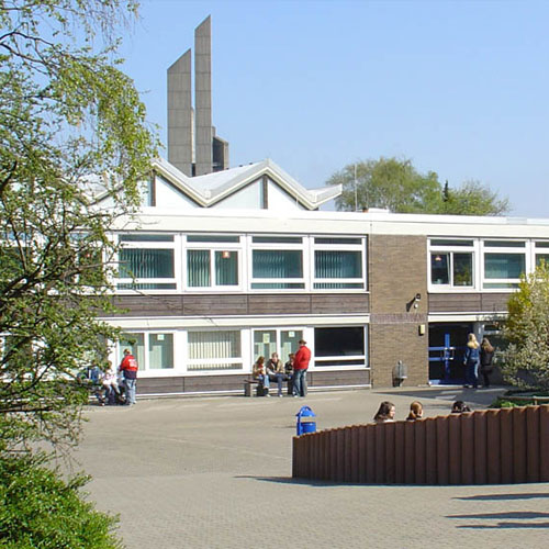 Blick auf den fast leeren, sonnigen Pausenhof und die Schulfassade. 