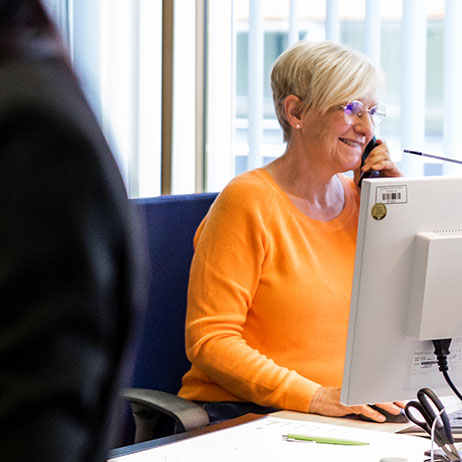 Schulsekretärin, Frau Lück, lachend in eine Telefonat vertieft, vor dem Computerbildschirm sitzend. 